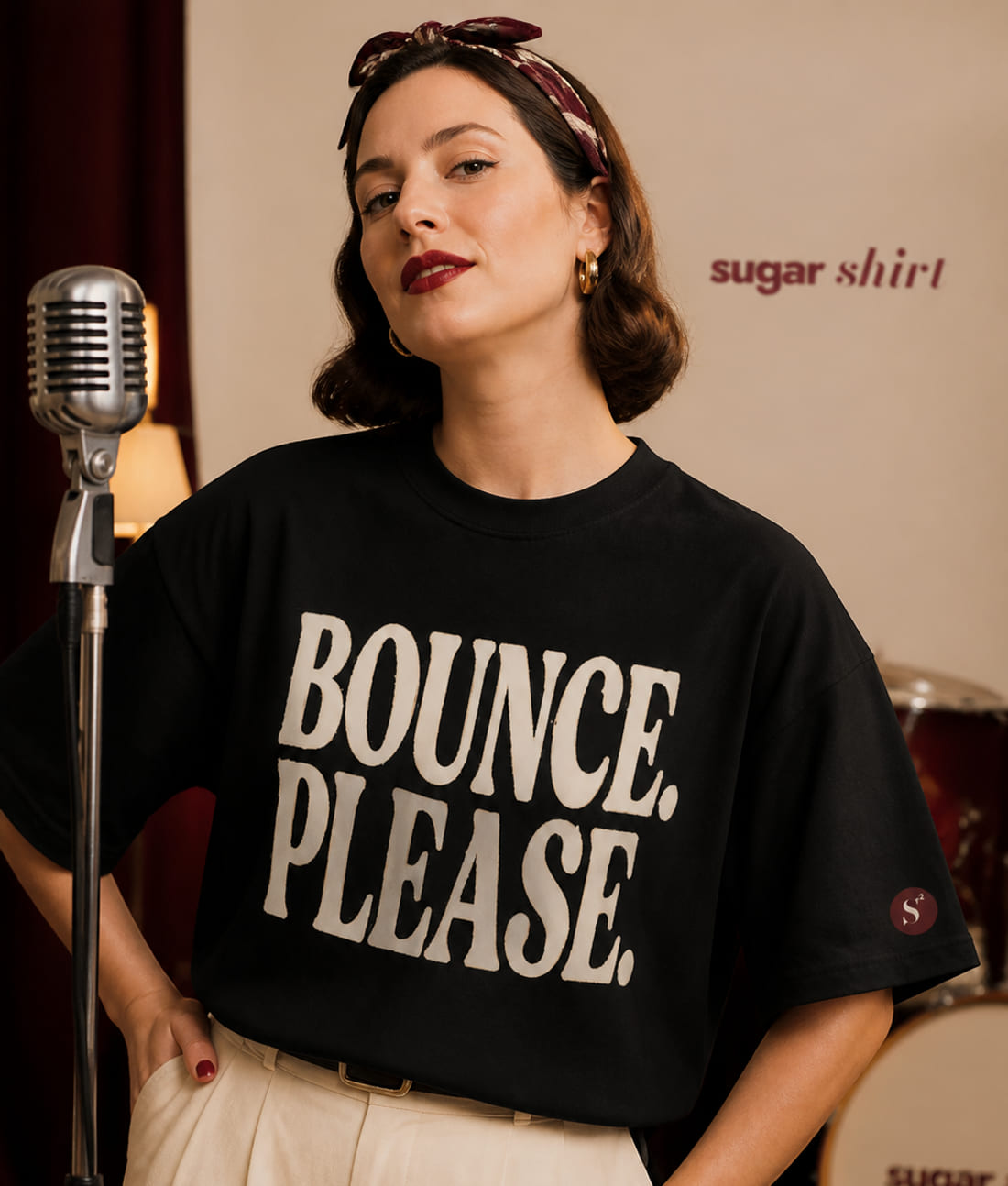 Cantante accanto a un microfono vintage con una batteria alle spalle, indossa la t-shirt Bounce. Please. nera