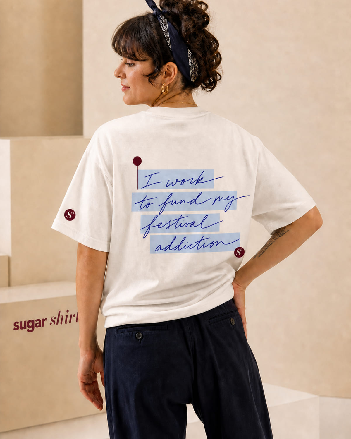 T-shirt oversize crema con la frase «I work to fund my festival addiction» scritta a mano su evidenziatore azzurro